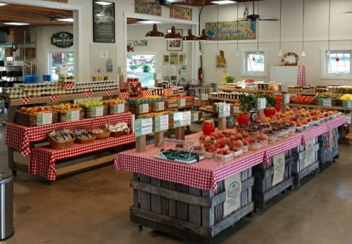 A vibrant market display with jars of preserves, fresh produce, and checkered tablecloths in a bright, inviting space.