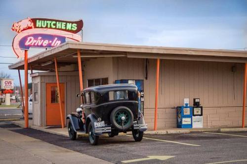 A vintage car parked outside Hutchens Drive-In, featuring a retro neon sign and a simple building facade.