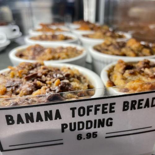 Close-up of banana toffee bread pudding in white ramekins, displayed behind a sign with the price of $6.95.