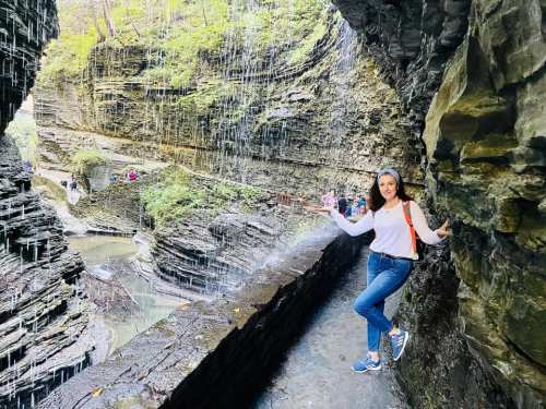 A person stands by a waterfall in a rocky canyon, surrounded by lush greenery and flowing water.