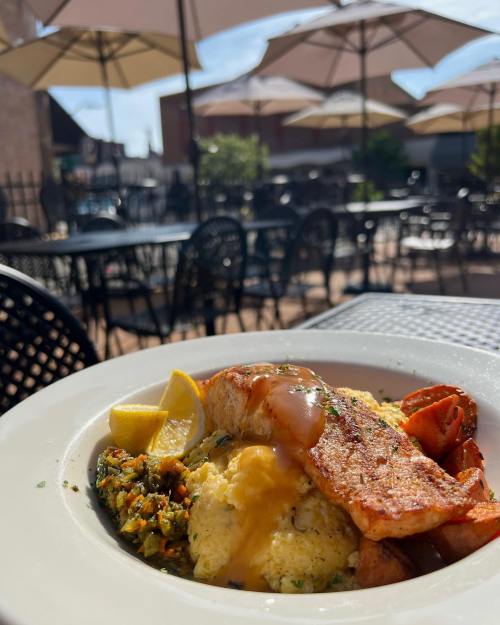 A plate of salmon with lemon, served with scrambled eggs and vegetables, set outdoors with umbrellas in the background.