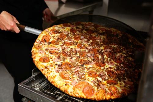 A person pulls a large, loaded pizza with pepperoni and sausage from an oven.