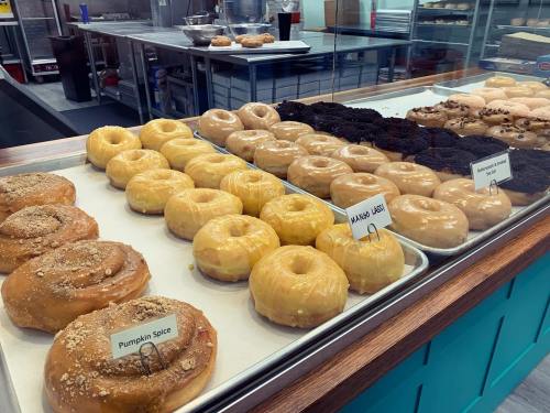 A display case filled with various donuts, including pumpkin spice and glazed varieties, in a bakery setting.