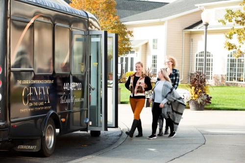 Three women walk towards a shuttle bus parked outside a building, smiling and carrying bags.