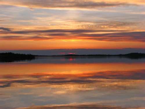 A serene sunset over a calm lake, with vibrant orange and purple hues reflecting on the water's surface.