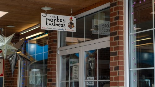 Sign for "A Little Monkey Business" store, featuring playful graphics, located in a brick storefront.