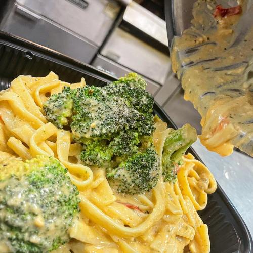 Creamy fettuccine pasta topped with broccoli and a rich sauce, served in a black takeout container.