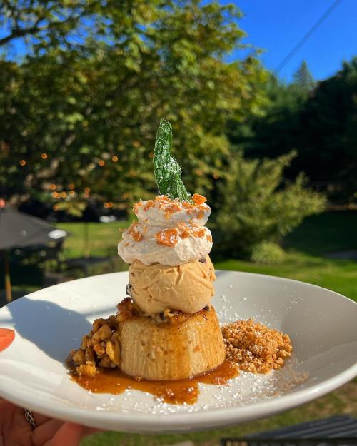 A dessert plate featuring flan topped with ice cream, whipped cream, and a mint leaf, surrounded by nuts and caramel drizzle.