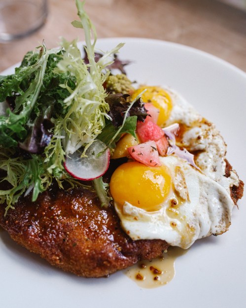 A plate featuring a crispy fried dish topped with two sunny-side-up eggs, fresh greens, and diced tomatoes.