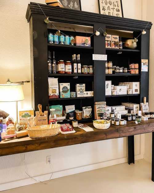 A wooden shelf displays various jars, bottles, and packaged goods in a cozy shop setting.