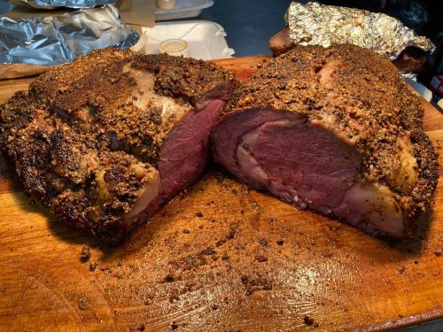 A perfectly cooked roast beef, seasoned and sliced, resting on a wooden cutting board.