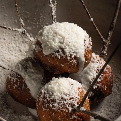 Four round pastries topped with white icing, resting in a bowl with a rustic twig arrangement.