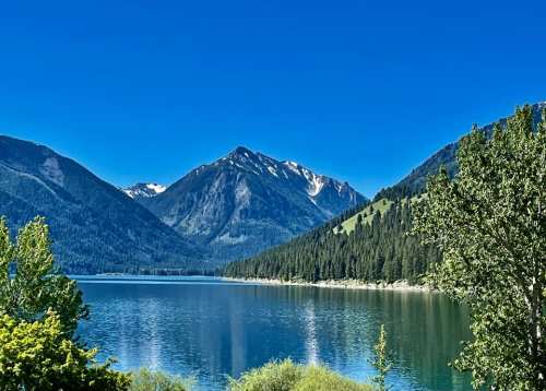 A serene lake surrounded by mountains and lush greenery under a clear blue sky.