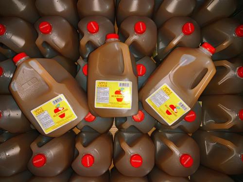 Several jugs of apple cider stacked together, each with a red cap and yellow label.