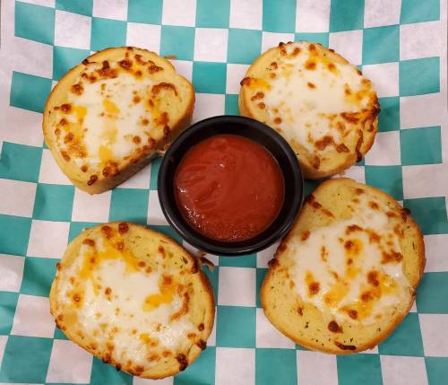 Four cheesy bread slices arranged around a small bowl of marinara sauce on a green and white checkered paper.