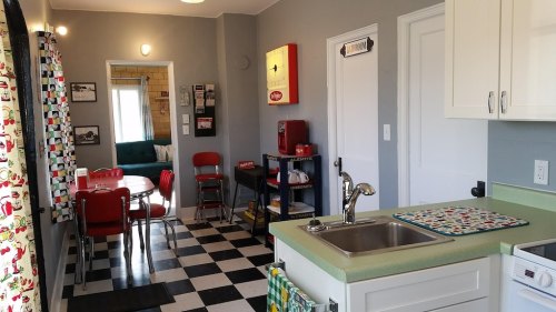 A bright kitchen with a green countertop, checkered floor, and a dining area featuring red chairs and a round table.
