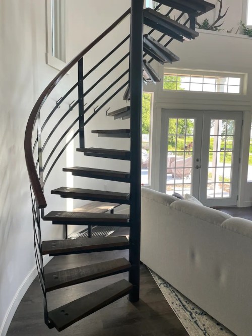 A modern spiral staircase with wooden steps and metal railing, leading to a bright, open living space.