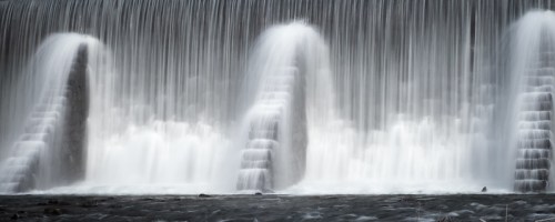 A serene waterfall cascading over a dam, creating a misty effect as water flows down in multiple streams.