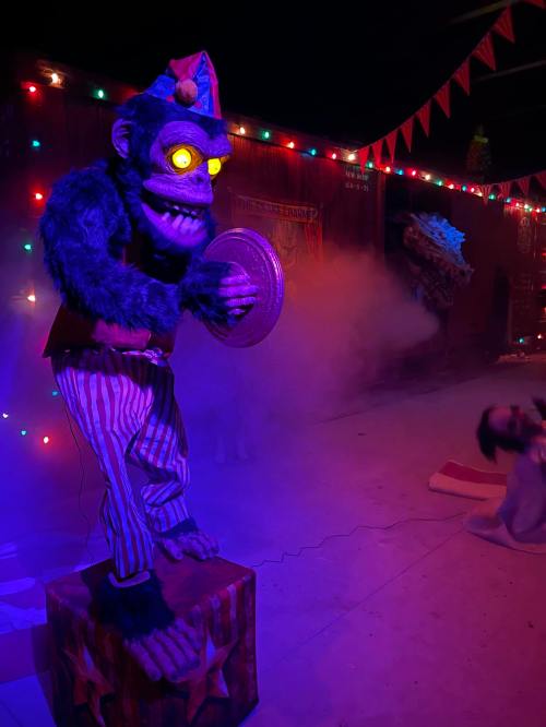 A colorful, animated monkey figure with glowing eyes stands on a pedestal, surrounded by festive lights and fog.