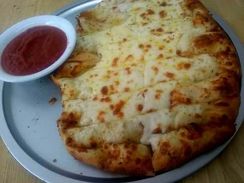 A large, cheesy flatbread served with a side of marinara sauce on a metal plate.