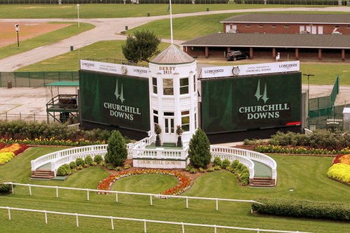 A view of Churchill Downs with a grandstand, flower beds, and large screens displaying the venue's name.
