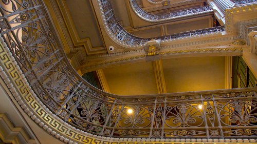 Intricate wrought iron railings and ornate architecture of a grand staircase, viewed from below.