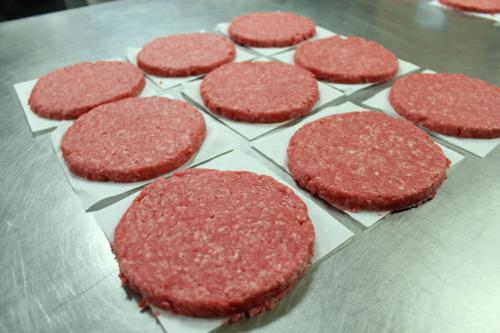 Nine raw hamburger patties arranged on parchment paper on a stainless steel surface.