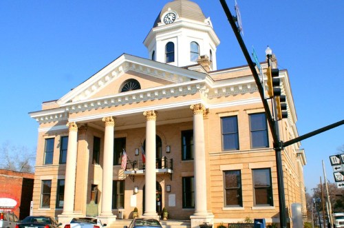 Historic courthouse with a clock tower, columns, and American flags, set against a clear blue sky.
