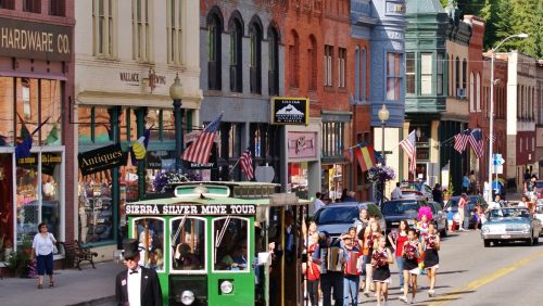 A bustling street scene with historic buildings, shops, and a green trolley, filled with people and American flags.
