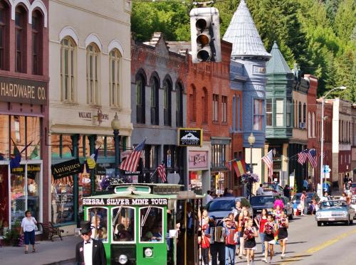 A bustling street scene with historic buildings, shops, and a green trolley, filled with people and American flags.
