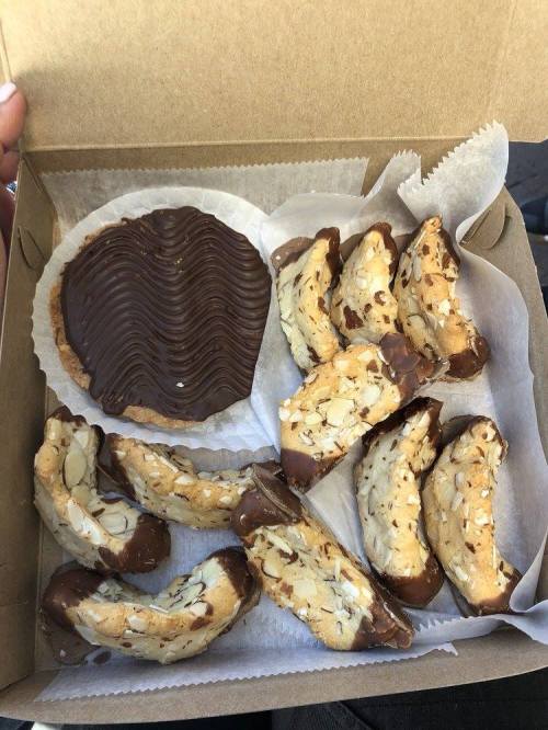 A box containing chocolate-dipped almond cookies and a round chocolate-covered dessert.