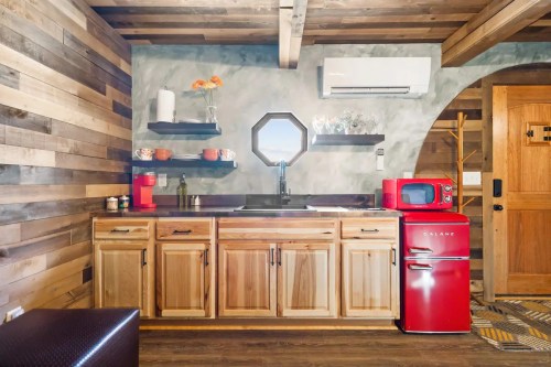 Cozy kitchen with wooden cabinets, a red retro fridge, and open shelves displaying plants and decor.