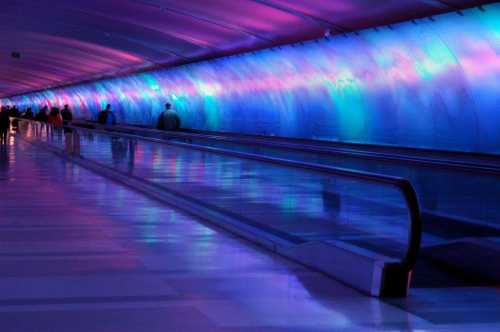 A brightly lit airport walkway with colorful blue and purple lighting, creating a vibrant atmosphere.