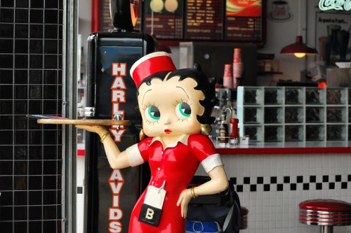 A vintage-style statue of a waitress in a red dress, holding a tray, in a retro diner setting.