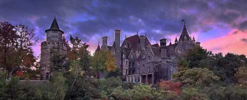 A grand, historic castle surrounded by trees, set against a colorful sunset sky.