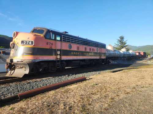 A vintage pink and silver train engine parked beside a row of tank cars on a sunny day.