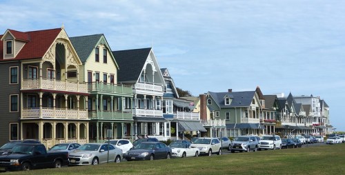 Colorful Victorian-style houses line a street, with parked cars and a cloudy sky in the background.