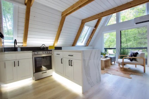 Modern kitchen with a sleek design, featuring a stove, white cabinets, and large windows overlooking greenery.