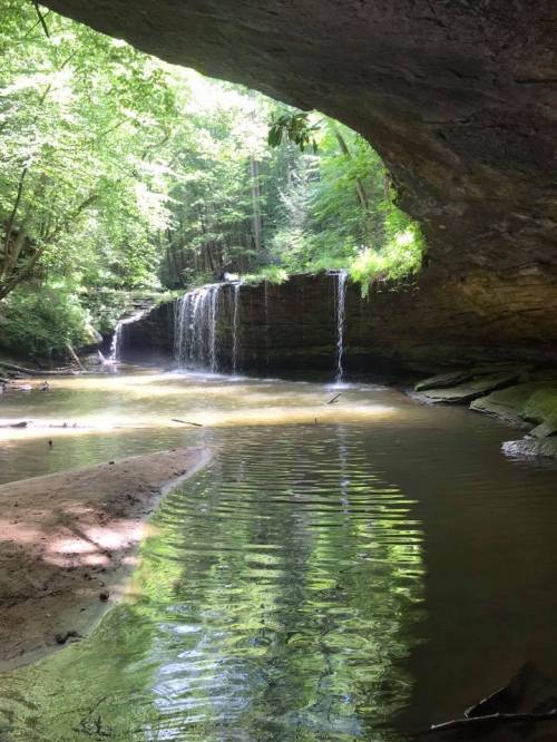 A serene scene of a waterfall cascading into a calm pool, surrounded by lush greenery and rocky formations.