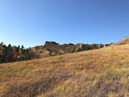 A scenic landscape featuring rolling hills, grassy fields, and a clear blue sky.