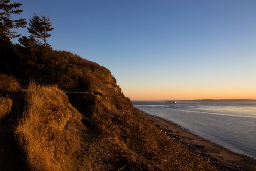 A serene coastal scene at sunset, featuring a sandy beach, gentle waves, and a distant ship on the horizon.