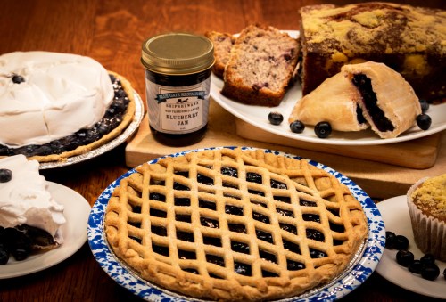 A table spread with blueberry pie, jam, muffins, and cakes, showcasing various blueberry desserts.