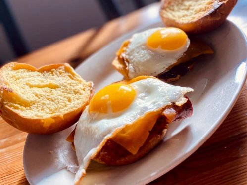 A plate with two toasted buns topped with fried eggs and melted cheese.