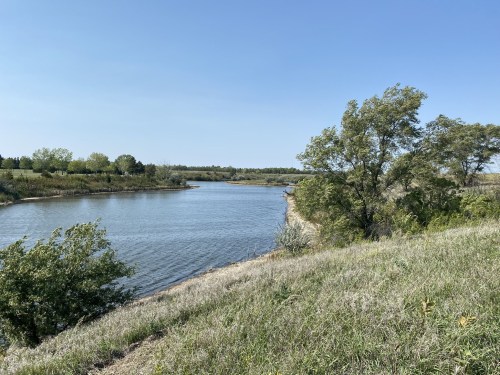 A serene river bends through a green landscape under a clear blue sky, with trees lining the banks.