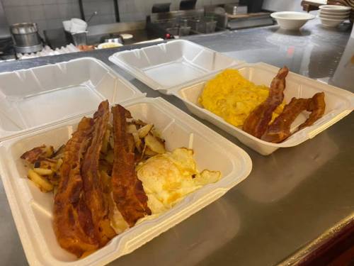 Two takeout containers: one with crispy bacon and hash browns, the other with scrambled eggs and more bacon.