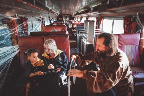 A bus interior decorated for Halloween, featuring a child and two adults in costumes, engaged in a fun activity.