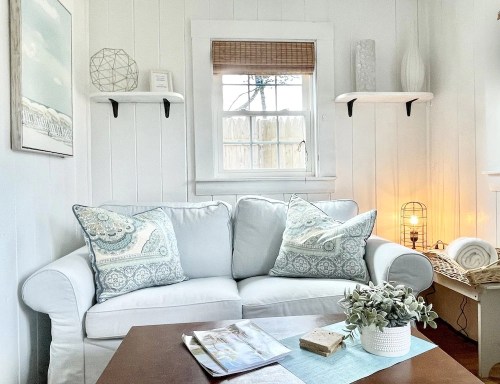 Cozy living room corner with a white couch, decorative pillows, a wooden table, and soft lighting.