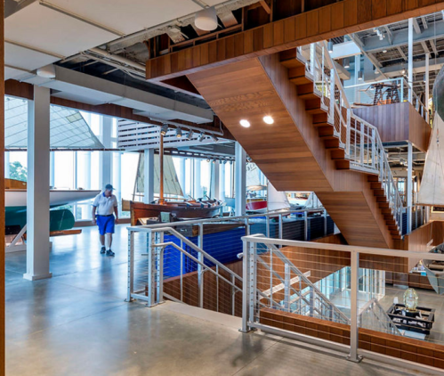 A modern interior of a maritime museum featuring wooden stairs and sailboats on display.