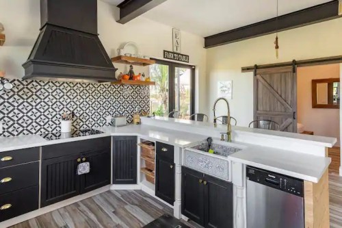 Modern kitchen with black cabinets, patterned backsplash, white countertops, and stainless steel appliances.