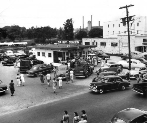 A busy Dairy Queen in the 1950s, with cars and people gathered around the iconic ice cream shop.